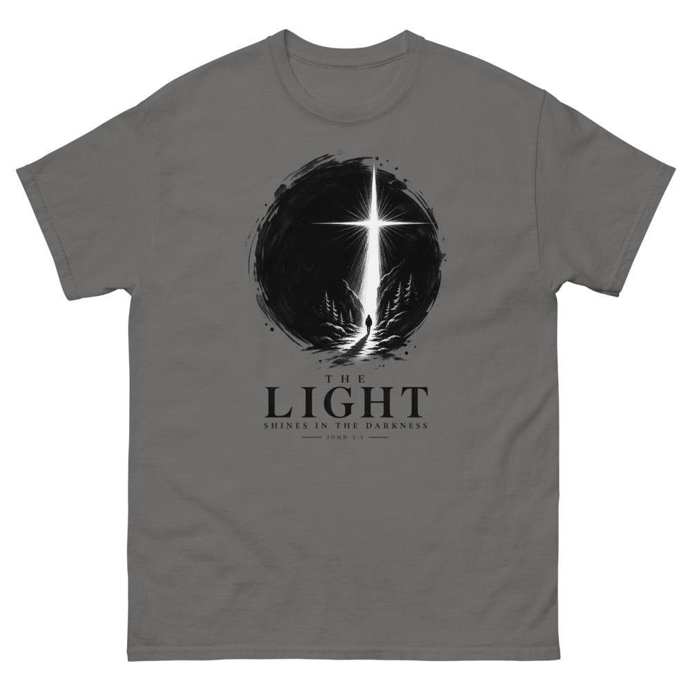 Ink circle with a figure walking toward a blazing cross reading The Light Shines In The Darkness on a Charcoal shirt