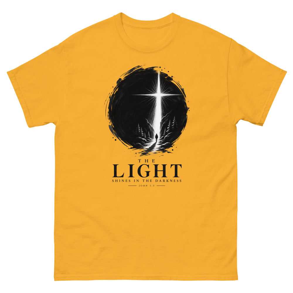 Ink circle with a figure walking toward a blazing cross reading The Light Shines In The Darkness on a Gold shirt