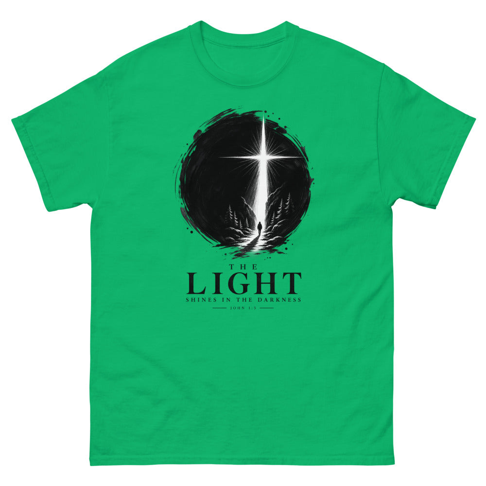 Ink circle with a figure walking toward a blazing cross reading The Light Shines In The Darkness on a Irish Green shirt