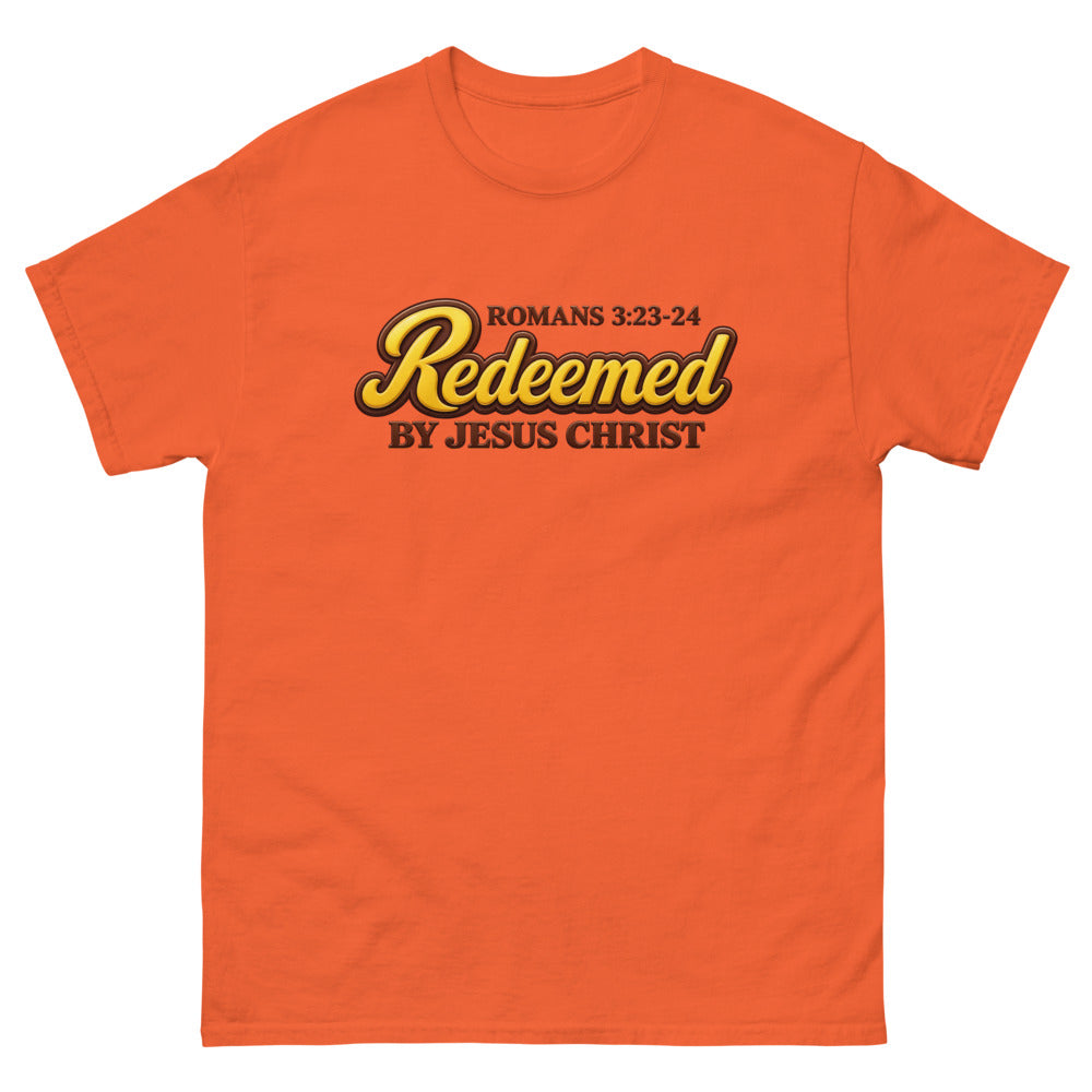 Glossy gold and brown candy script reading Redeemed by Jesus Christ, Romans 3:23-24 on a Orange shirt