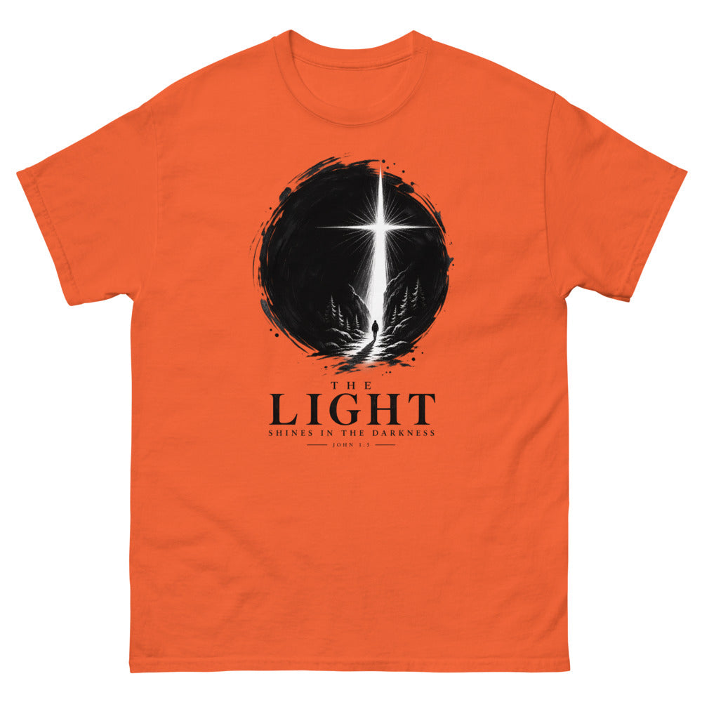 Ink circle with a figure walking toward a blazing cross reading The Light Shines In The Darkness on a Orange shirt