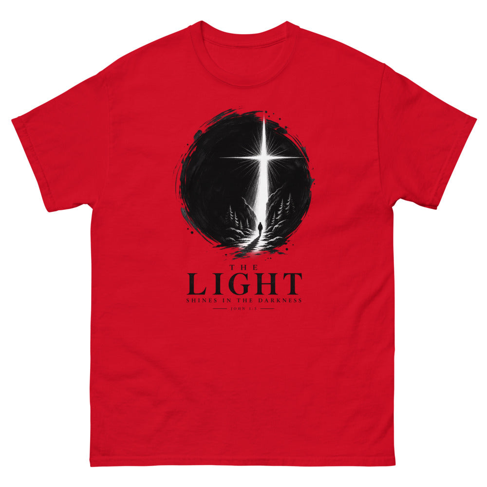 Ink circle with a figure walking toward a blazing cross reading The Light Shines In The Darkness on a Red shirt
